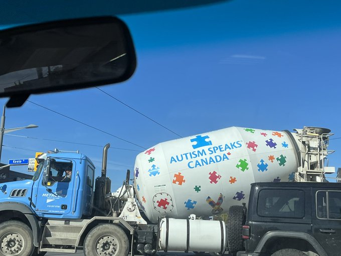 Photo out of a car windscreen, facing a cement mixer. 
					The cab is blue and the barrel bit is white. Emblazoned on the
					barrel are lots of colorful puzzle pieces and the
					Autism Speaks Canada logotype.