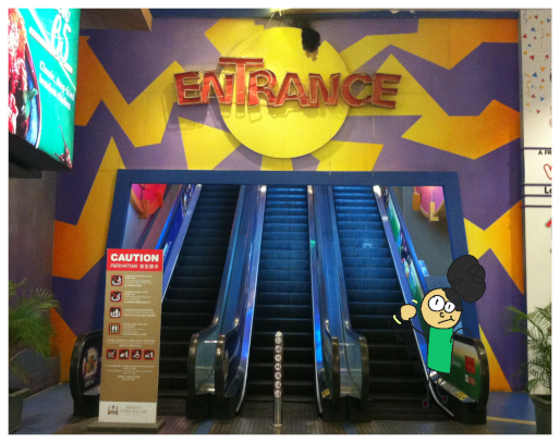 [This looks stupid without the photo ROTFL, sorry.
				Real life image of a funky 2000s entrance, slightly dilapidated. I drew myself on the right, waving with a blank expression.
				Behind, three escalators rise out of view.]