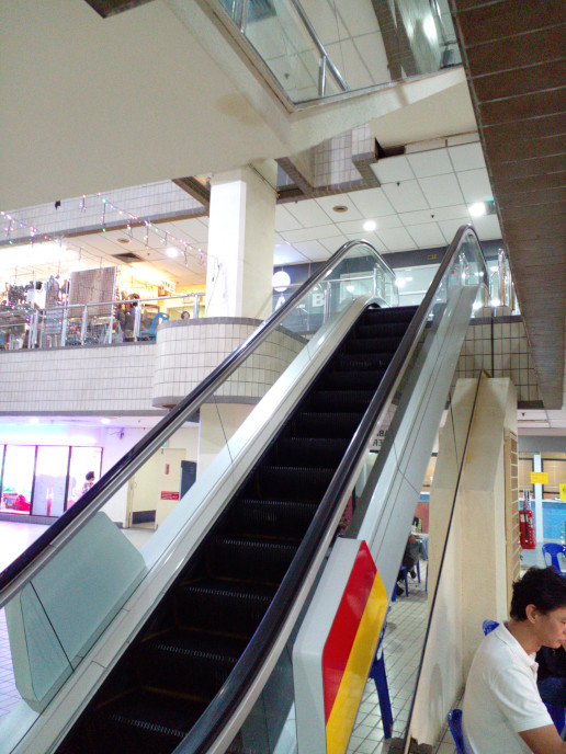 Now: As of when the image was taken, nobody was using the escalator. It now goes down. The stage has been
					removed revealing a single double pair of fire doors leading to the smoke lobby. One is wedged open.